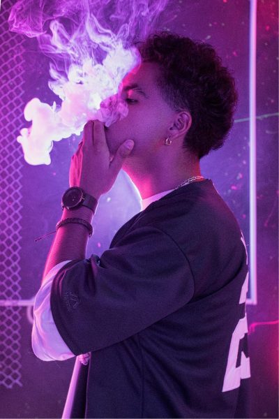 A young male vaping with a cloud of smoke out of his mouth.